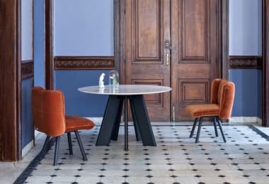 Round ceramic top dining table with lacquered base and upholstered orange chairs set